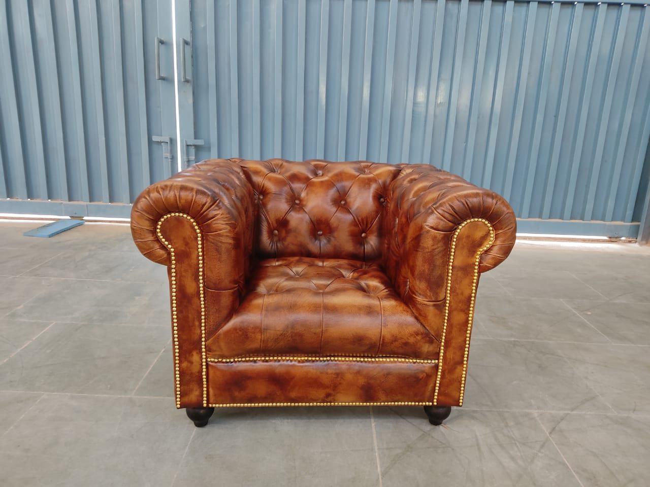 A finished Chesterfield armchair with a deep-buttoned bench seat in antiqued brown leather, brass stud trim along the arm fronts and base