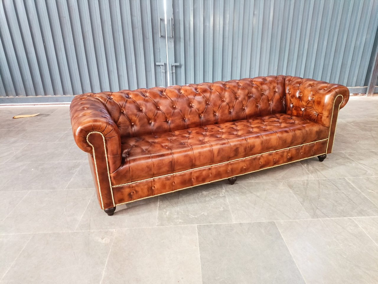 A finished four-seater Chesterfield with a continuous deep-buttoned bench seat in antiqued brown leather, three-quarter view