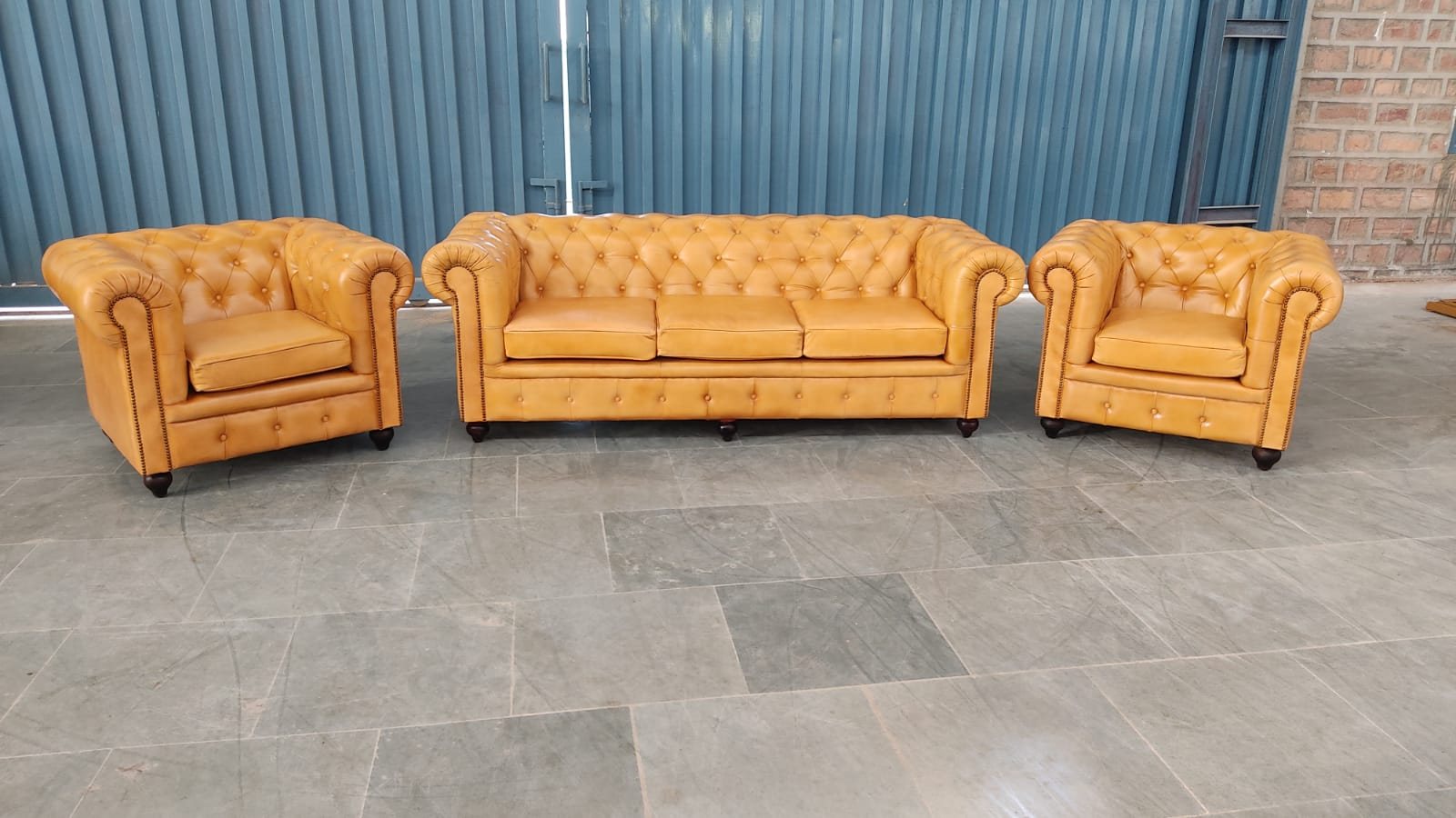 A finished three-piece Chesterfield suite — three-seater and two armchairs — in tan leather, standing completed on the workshop floor