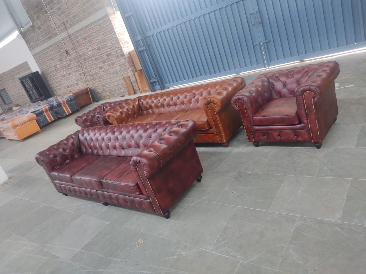 Several finished Chesterfield suites in oxblood and tan leather, standing completed with wrapped stock behind them