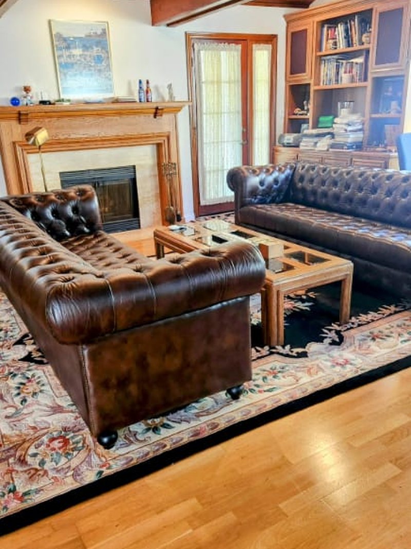 Customer photograph: two dark brown buttoned leather Chesterfields facing each other across a coffee table in a beamed room with a stone fireplace